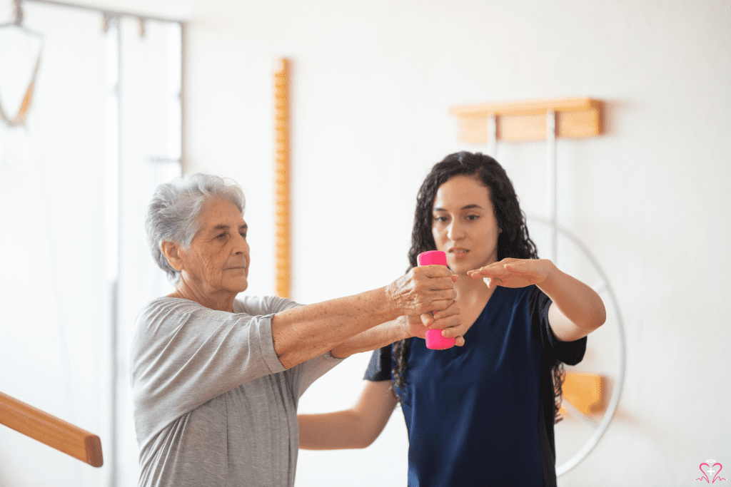 A physical therapy assisting an elderly woman with exercises using a pink dumbbell.