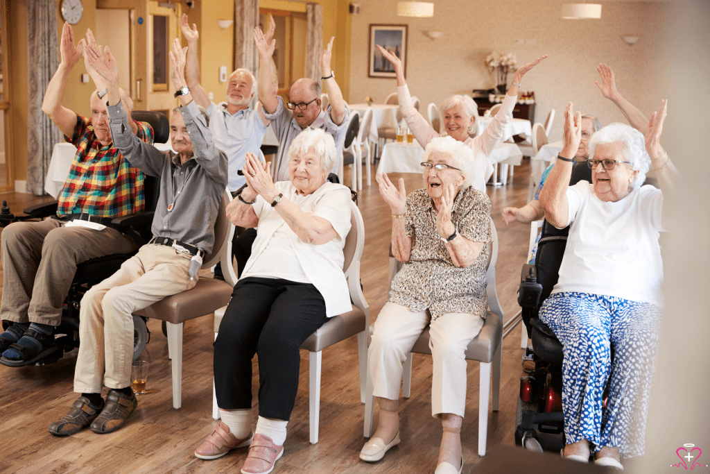 Community-Based Adult Services - A group of senior adults sitting in chairs, smiling, and raising their hands in a community activity room.