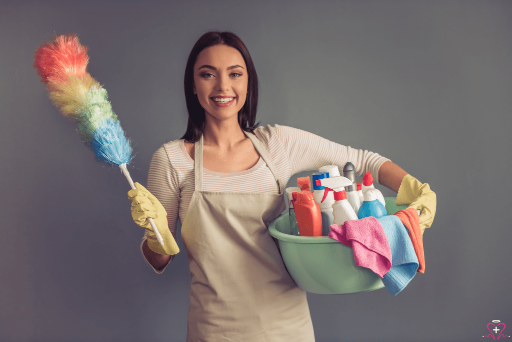 Smiling woman holding cleaning supplies and a feather duster, ready for homemaker services.