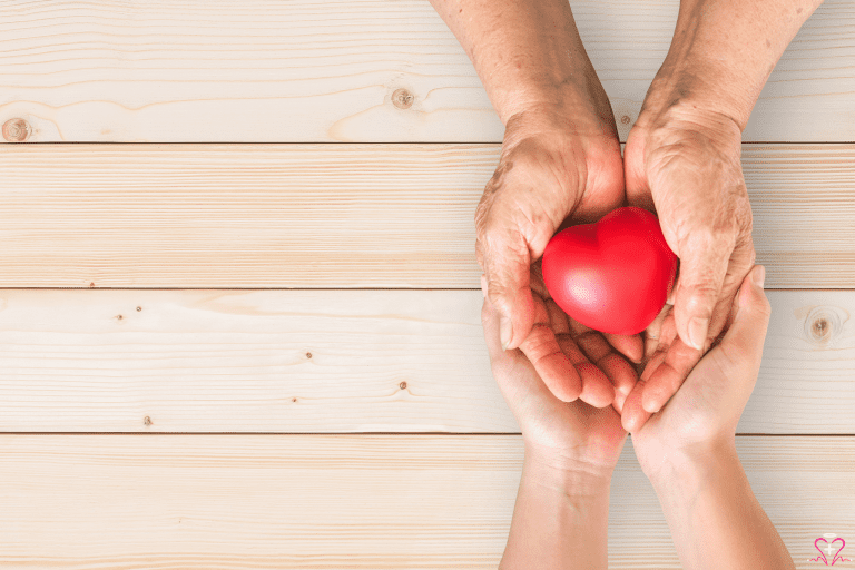 Understanding the Role of Palliative Care - Elderly hands holding a red heart model, symbolizing care and compassion, with younger hands supporting underneath.