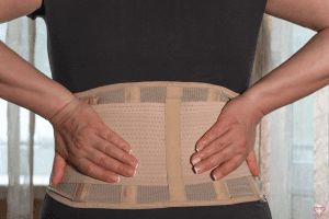 Back Brace - A close-up image of a person wearing a beige back brace for support, with hands placed on the lower back.