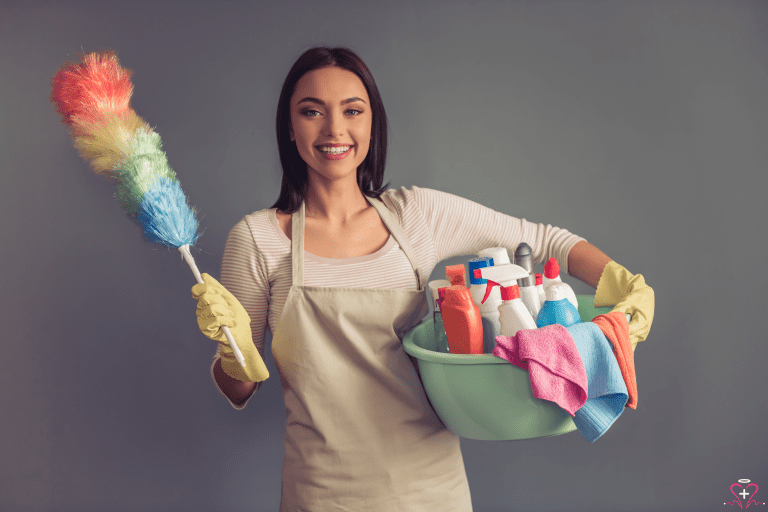 Smiling woman holding cleaning supplies and a feather duster, ready for homemaker services.