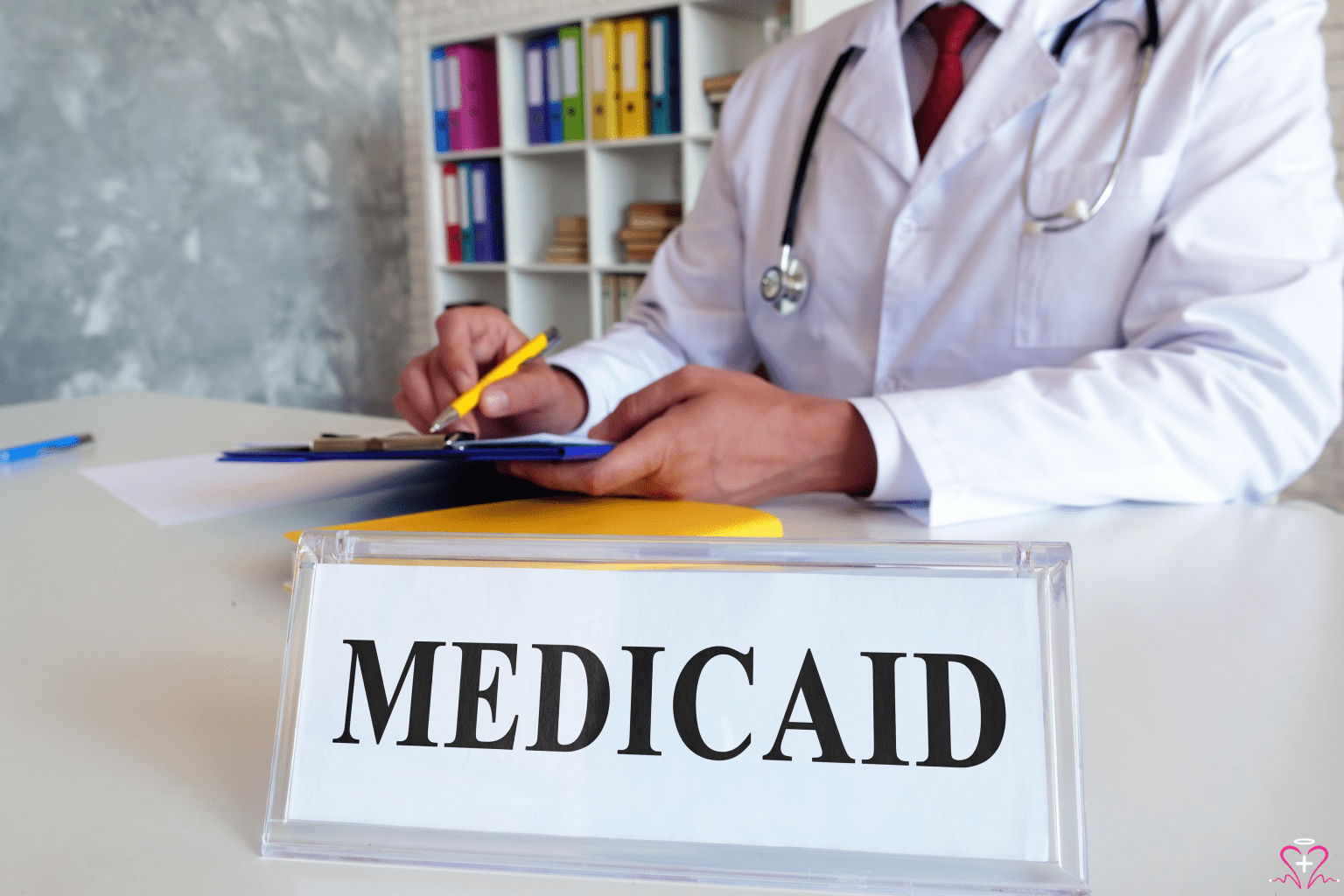 Medicaid Applications - A doctor filling out paperwork with a sign that says "Medicaid" on the desk.