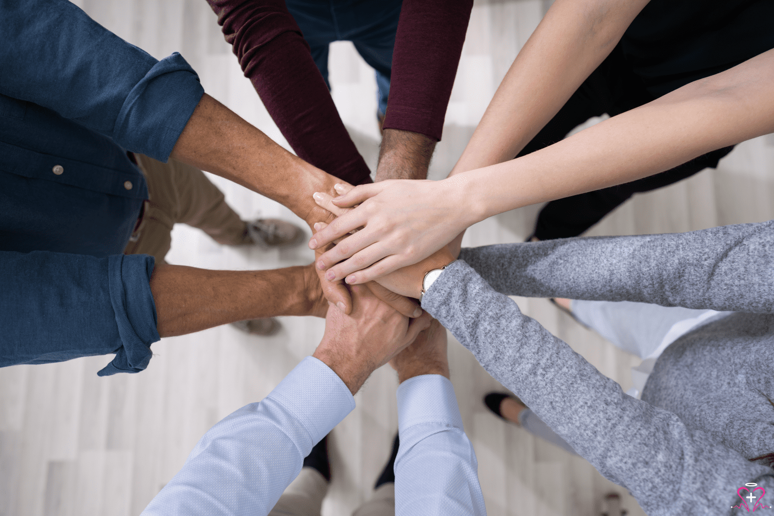 A diverse group of people standing in a circle, stacking their hands together in a show of unity and teamwork.