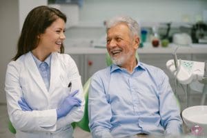 A senior man smiles while sitting next to a friendly dentist during his dental appointment, symbolizing affordable dental care.