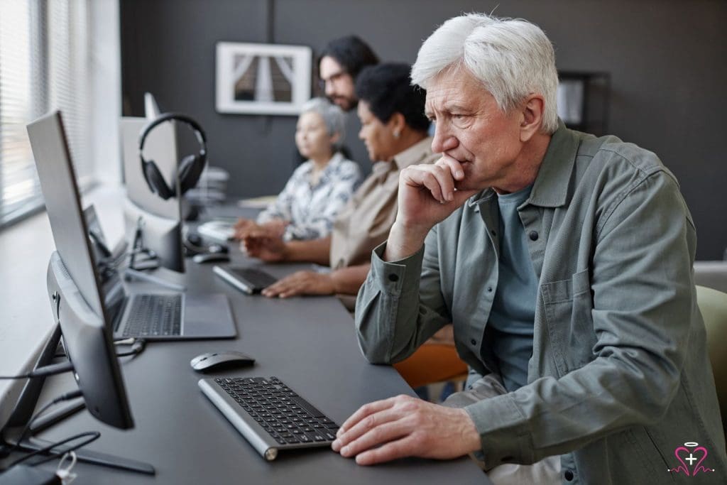 Senior man concentrating on computer work, part of a group engaged in digital skills training, a key initiative of the Senior Community Service Employment Program.