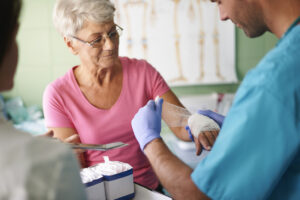 Healthcare professional wrapping a bandage on a senior woman’s hand, representing diabetic wound care services for seniors focused on healing and infection prevention