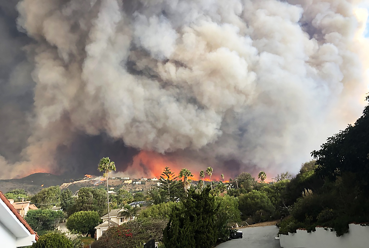 Massive wildfire burning in the hills near Los Angeles homes with thick smoke clouds, representing the 2018 Woolsey Fire crisis