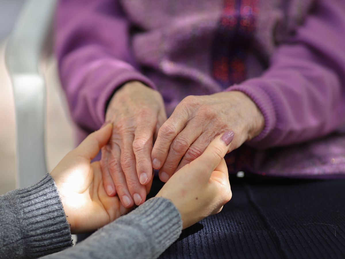 Caregiver gently holding senior’s hands during hospice care, symbolizing comfort and compassion — All Seniors Foundation