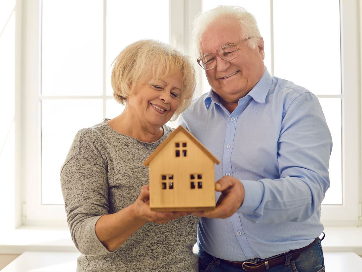 Smiling senior couple holding a model house, representing safe and accessible home modifications for aging in place.