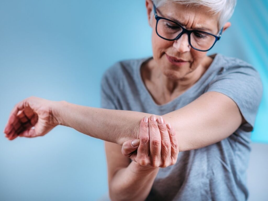 Senior woman holding her elbow in pain – elbow pain treatment and arthritis care for seniors in Los Angeles.