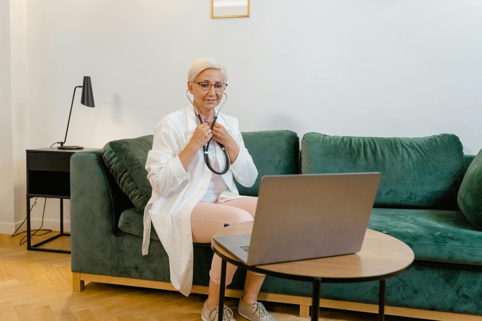 Female doctor in a white coat conducting an online consultation from home using a laptop.