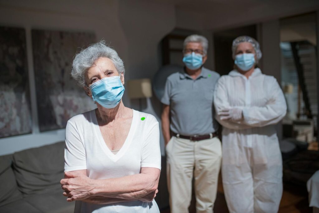 Healthcare workers in protective gear assisting elderly people indoors, highlighting COVID-19 care.