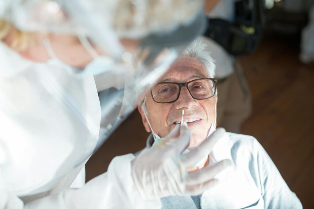 Elderly man receiving a nasal swab test from a healthcare professional in a clinical setting.