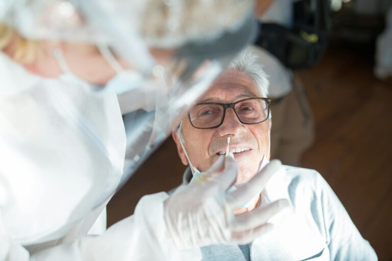 Elderly man receiving a nasal swab test from a healthcare professional in a clinical setting.