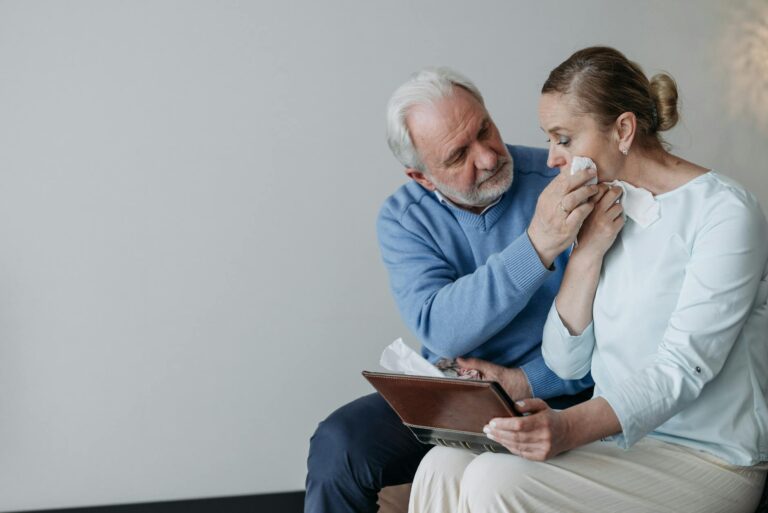 A senior couple embracing and wiping away tears while reminiscing with a photo album.