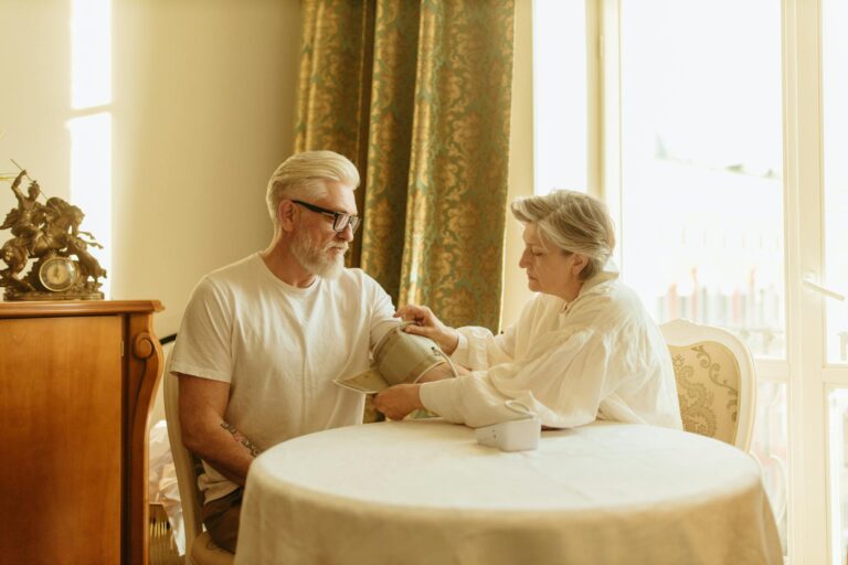 Una pareja de ancianos se controla la presión arterial con un tensiómetro digital en la mesa de su casa.