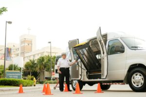 A security guard operates a wheelchair lift on a van outside a medical facility.