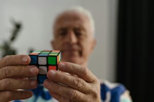 A senior adult man solving a Rubik's Cube, focusing on the puzzle with determination.