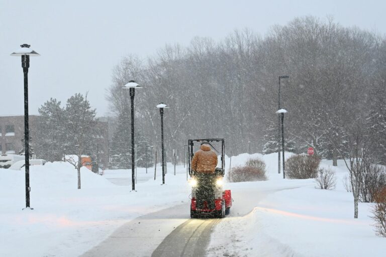 A snow plow clearing a path through heavy snowfall in a winter landscape.